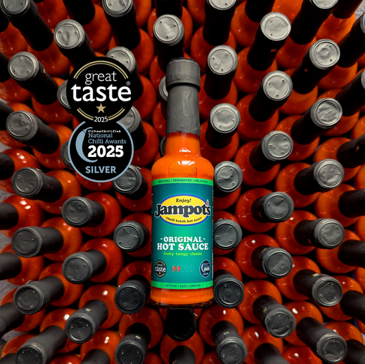 A bottle of Jampot's Original Hot Sauce centered against a dense background of many red hot sauce bottles with black caps. Two award badges on the left read 'great taste 2025' and 'Innovation and Excellence Chili Awards 2025 SILVER'.